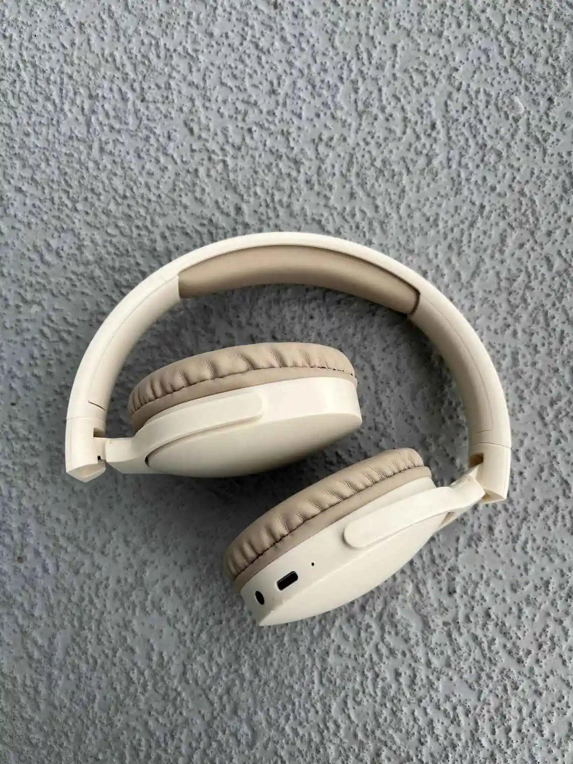 Foldable wireless over-ear headphones in cream color with cushioned ear pads and adjustable headband for comfort.