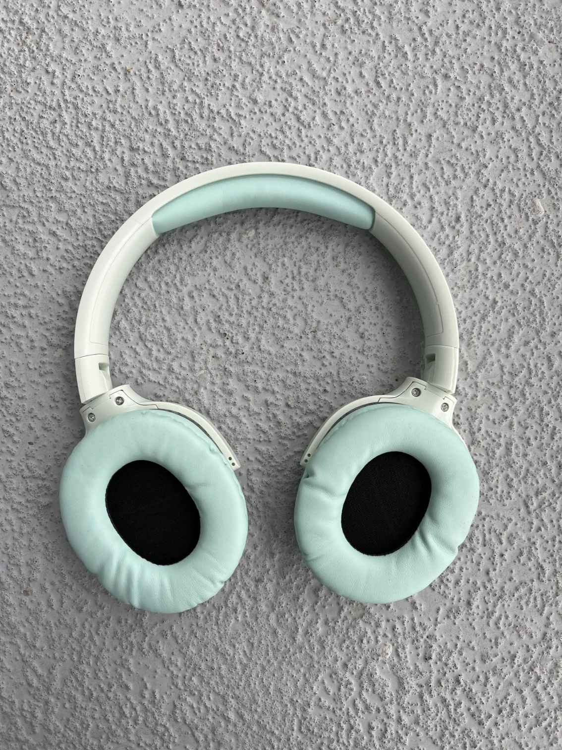 Green mint Bluetooth headphones with soft ear cushions, shown on a textured gray surface for a modern and stylish look.