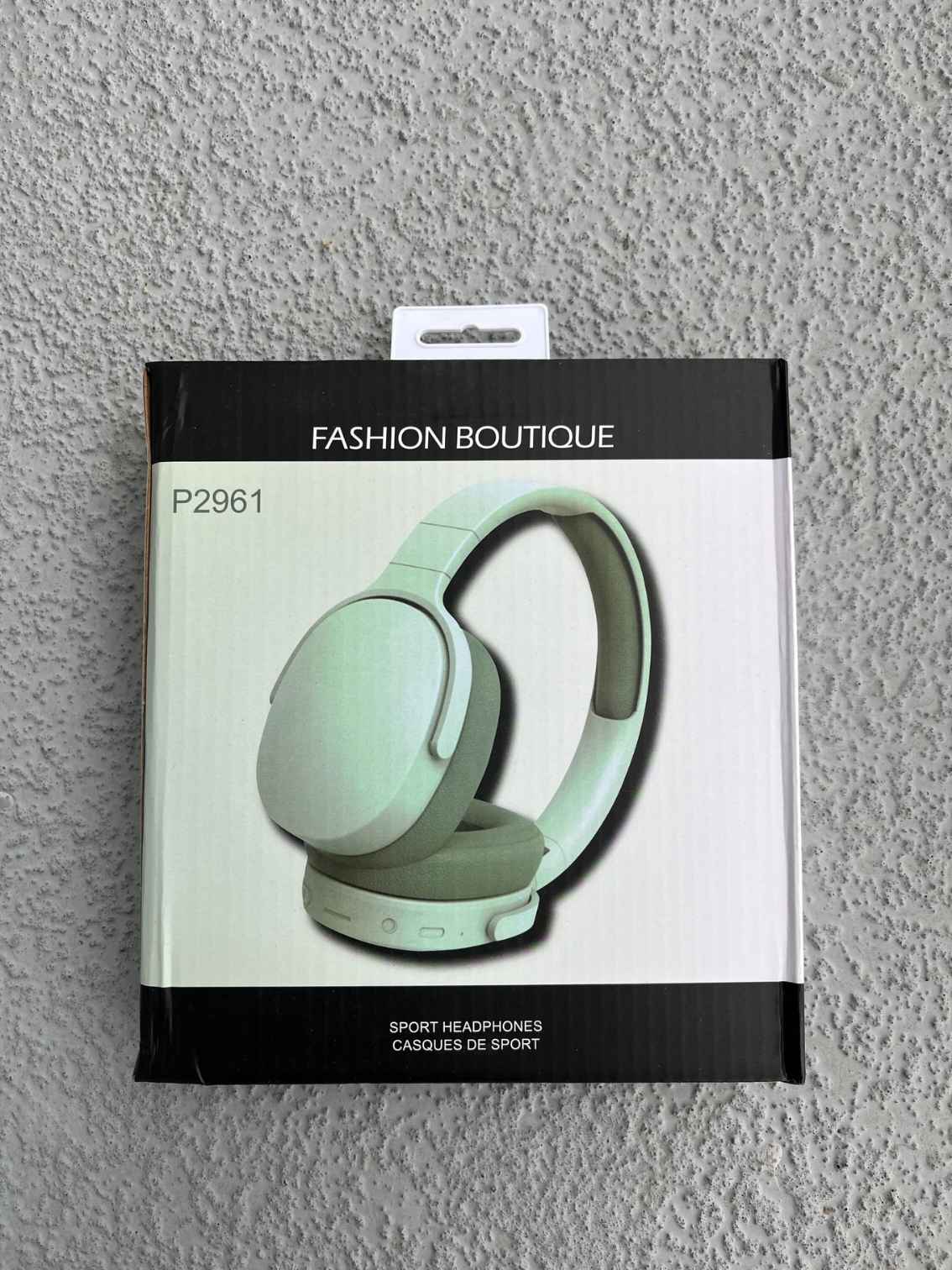 Bluetooth headphones in mint green packaging displayed on a textured gray background.