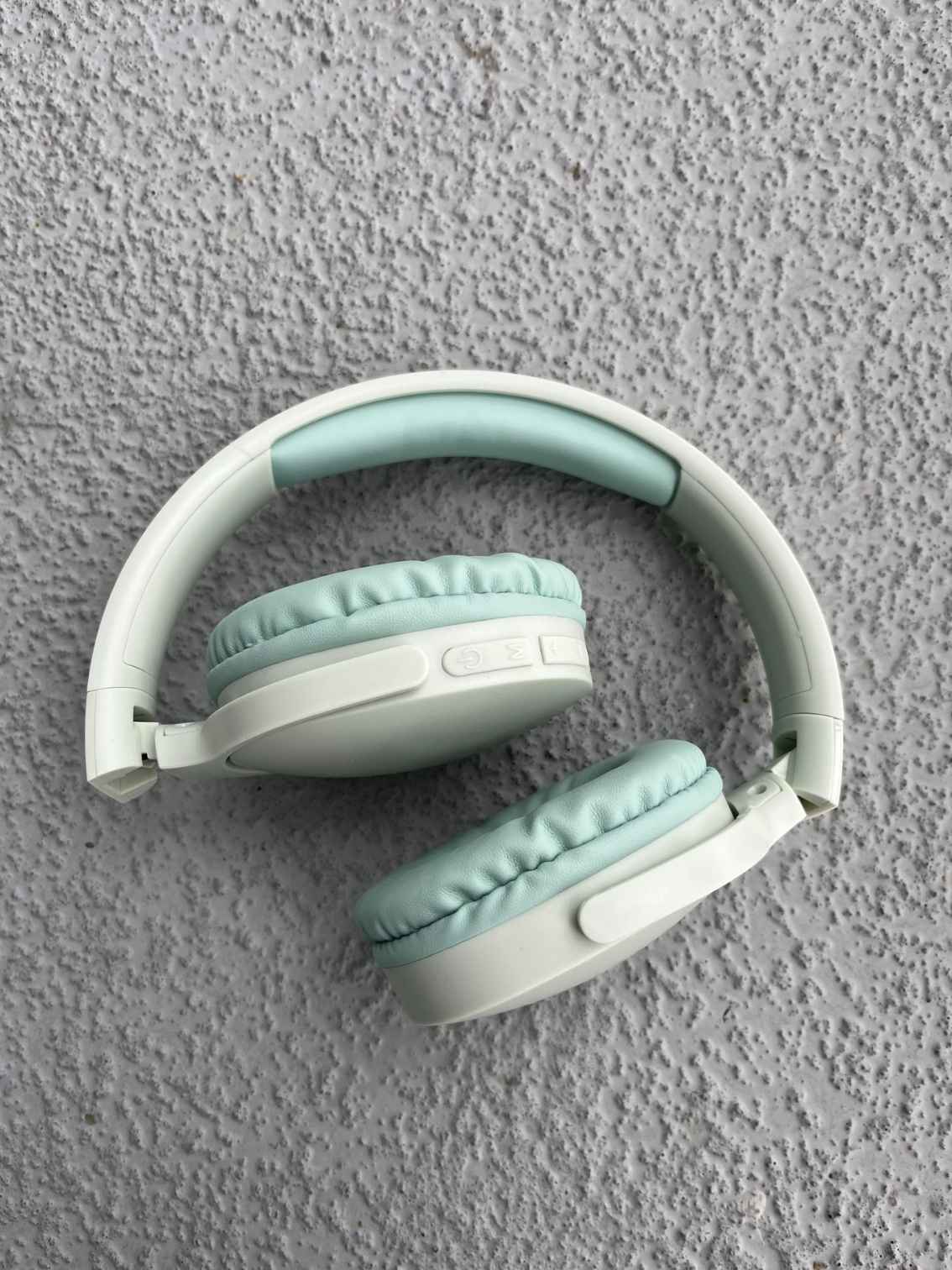 Folded green Bluetooth headphones with soft ear padding, showcased on a textured gray surface for compact storage and comfort.