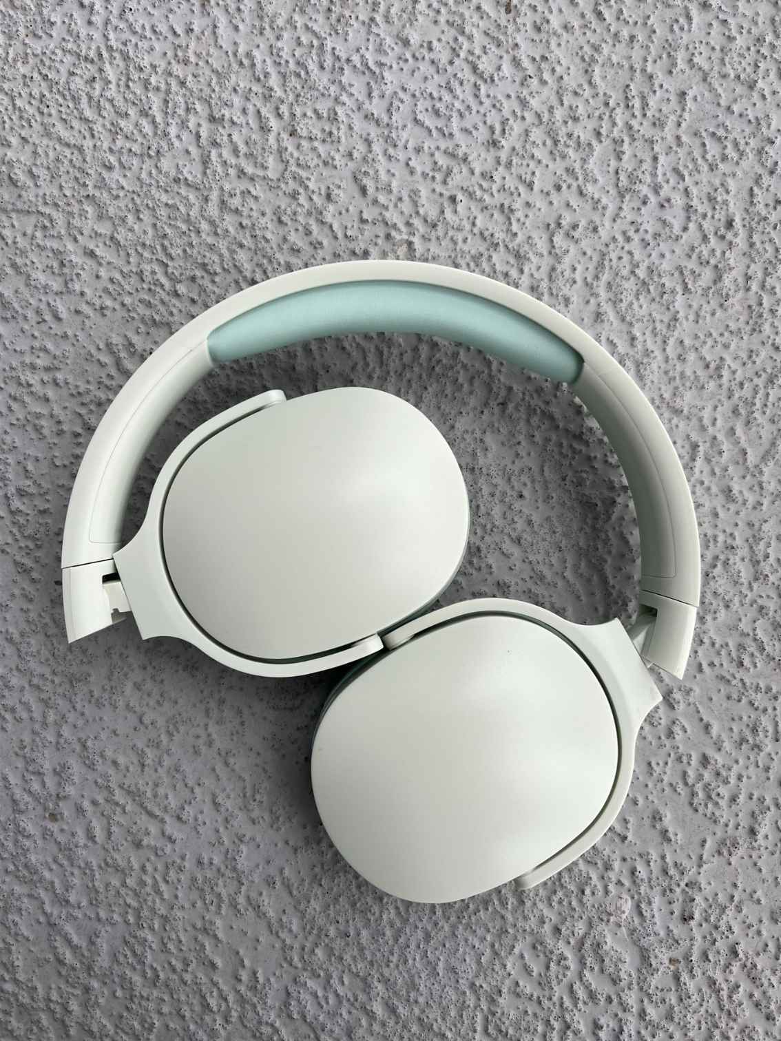 Folded mint green Bluetooth headphones with a sleek, portable design, displayed on a textured gray background.