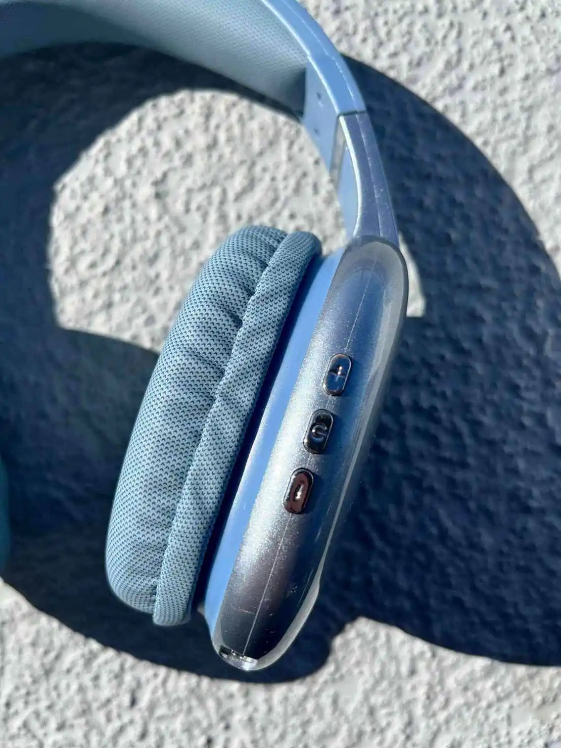 Close-up of control buttons on the side of PG02 blue wireless Bluetooth headphones with soft ear cushions.