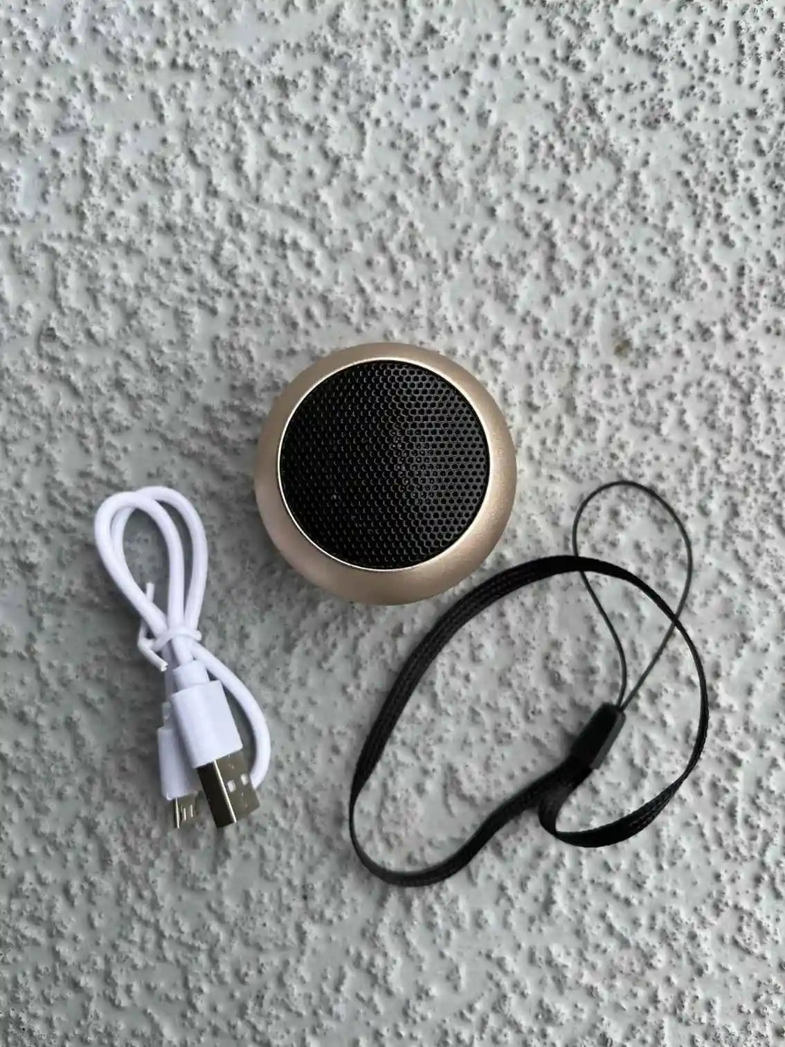 Mini rose gold Bluetooth speaker with accessories.