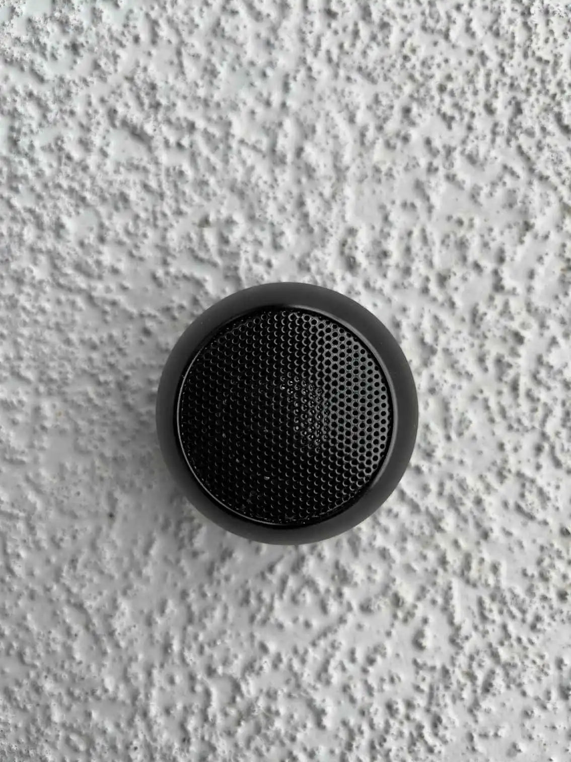 Mini Bluetooth speaker in black on a textured surface.