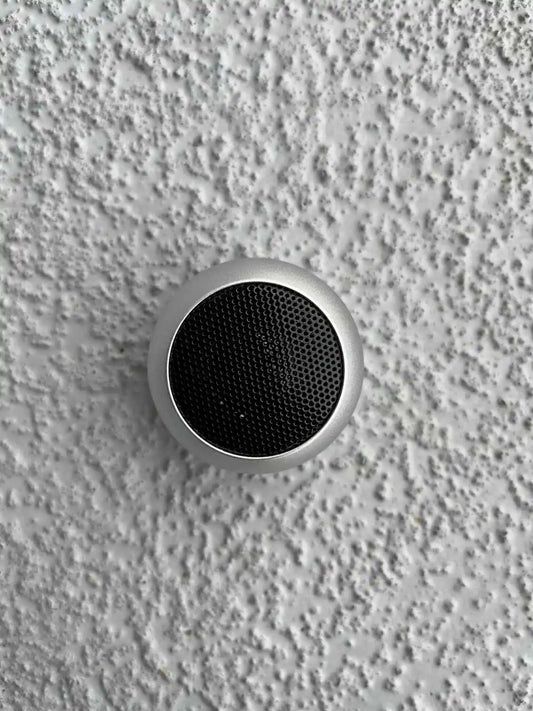 Mini silver Bluetooth speaker on a textured surface.