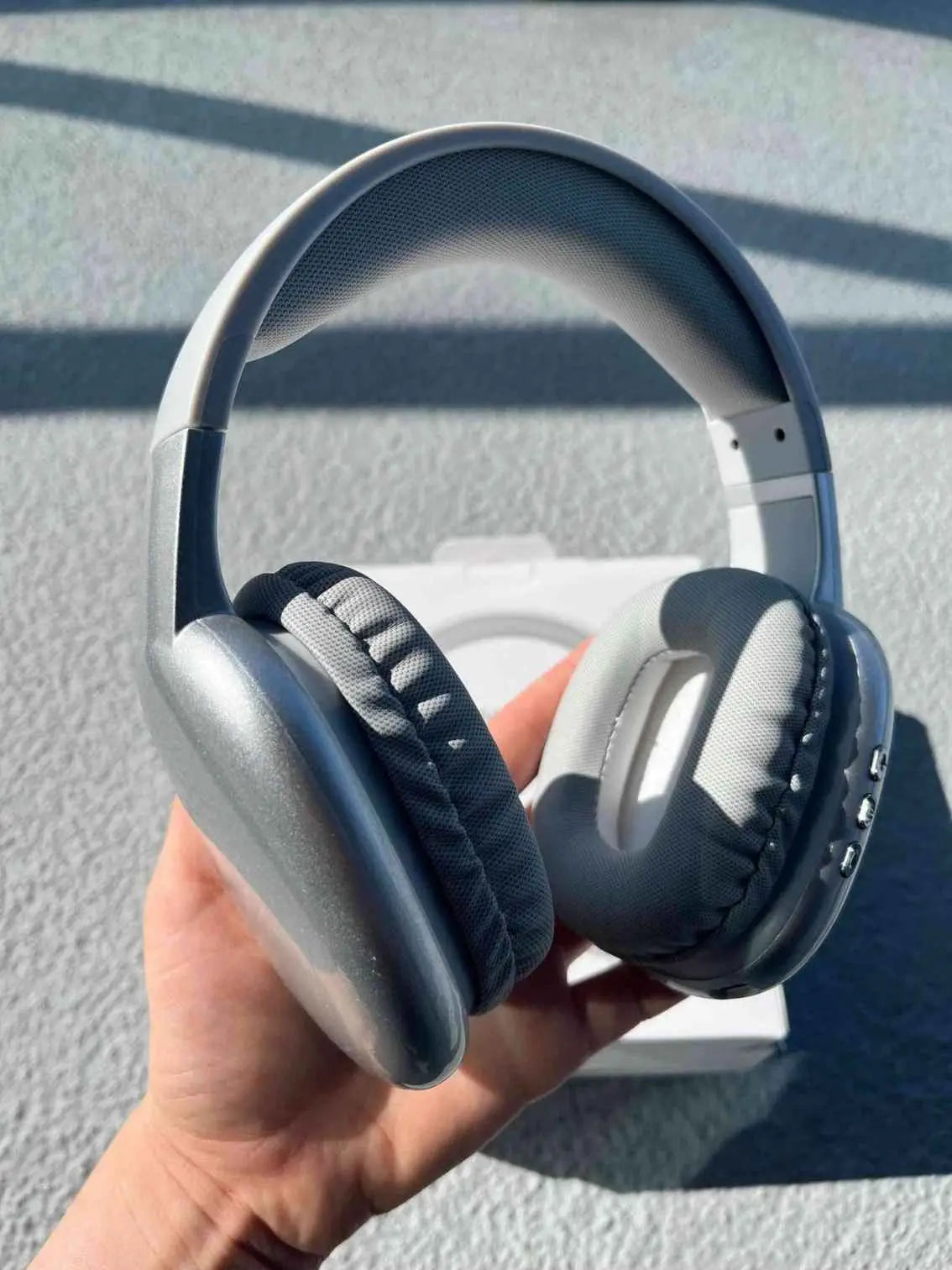 Silver Bluetooth PG02 wireless headphones are held in hand from a different angle.