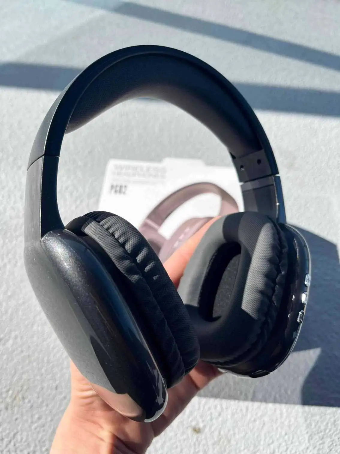 Black PG02 wireless headphones are held in hand from a different angle.