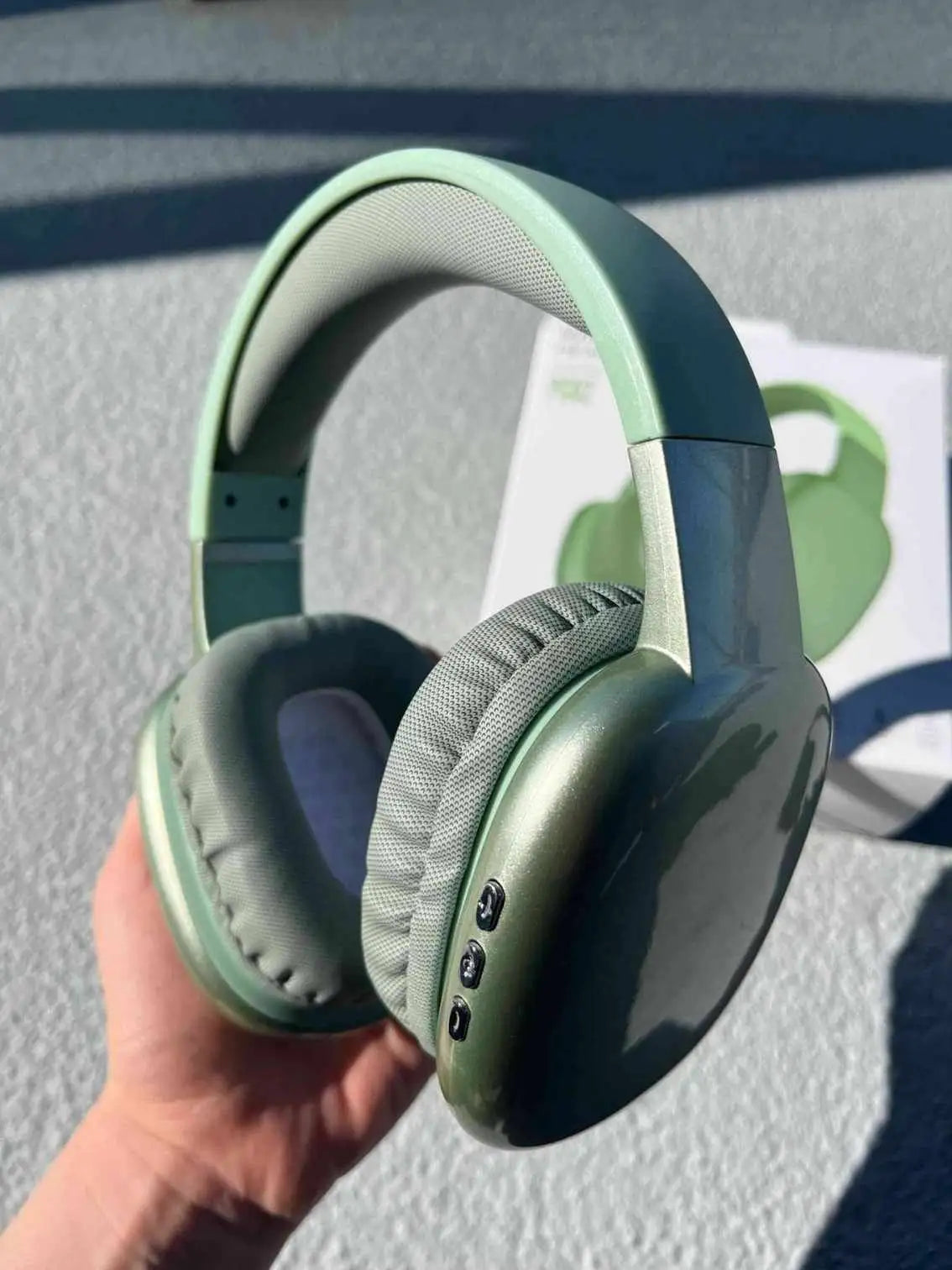 Green wireless PG02 Bluetooth headphones with cushioned ear pads, held in hand, with product box in the background.