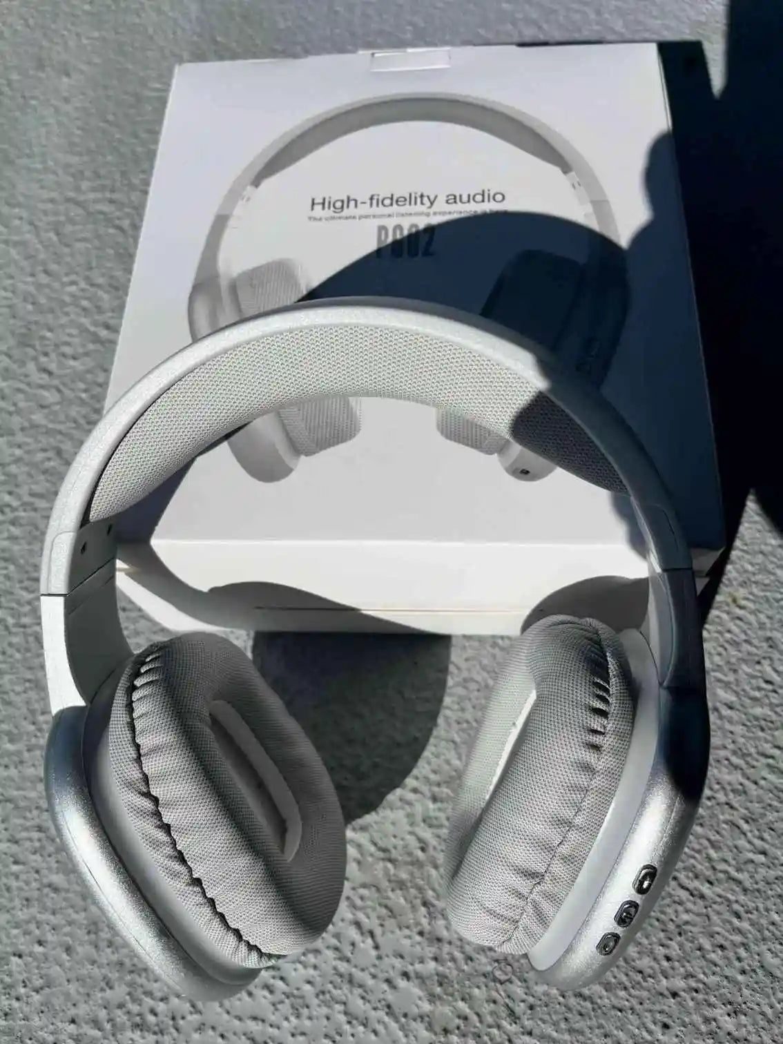 Silver wireless PG02 Bluetooth headphones with soft ear cushions, displayed in front of product packaging.