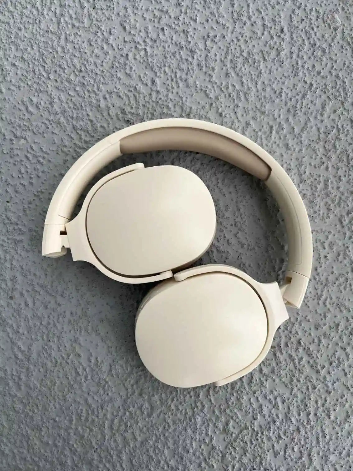 Compact foldable wireless headphones in cream color with sleek over-ear design for portability and comfort.