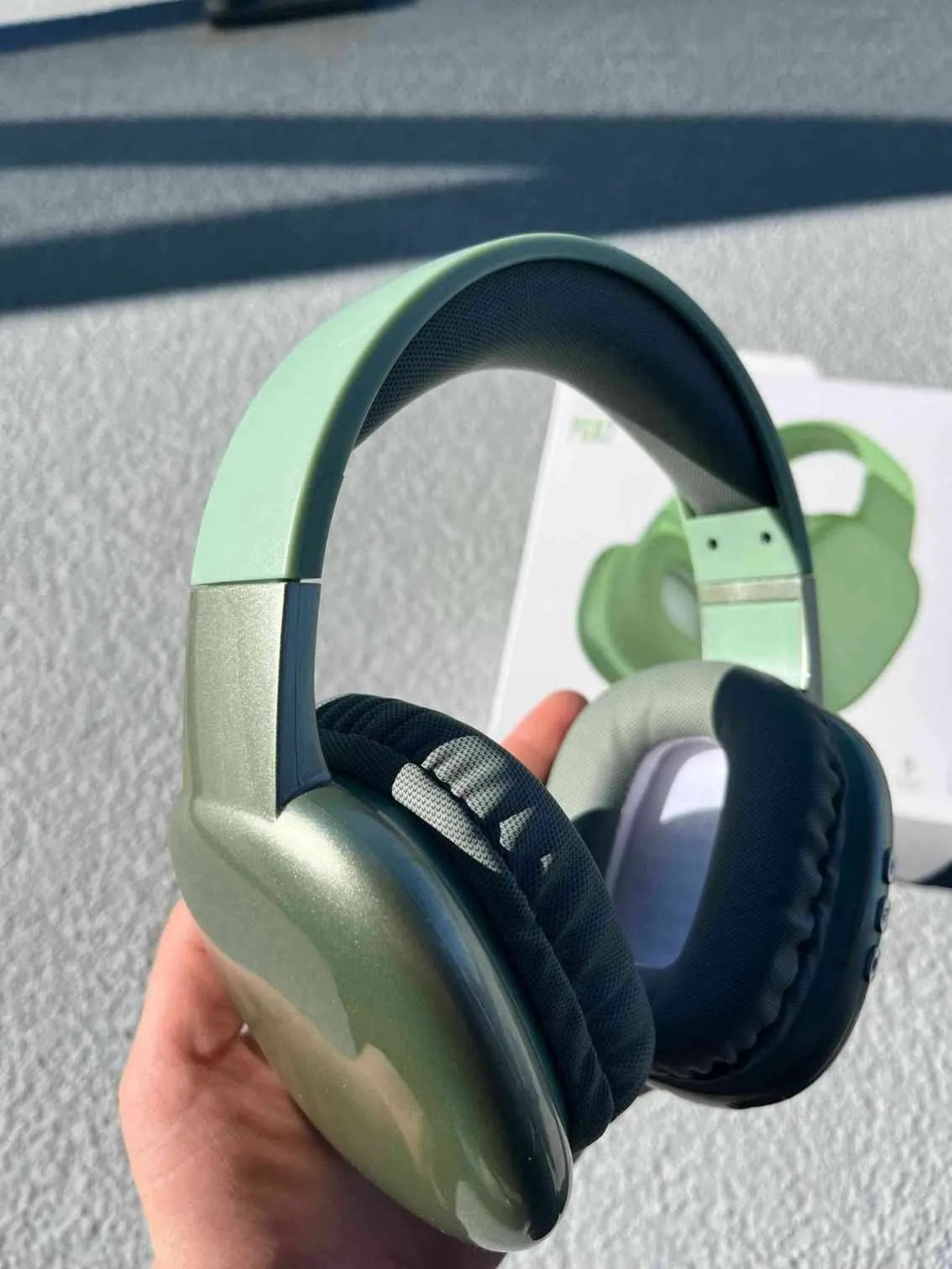 Green over-ear Bluetooth PG02 headphones with soft cushions and control buttons held in hand with packaging in the background.