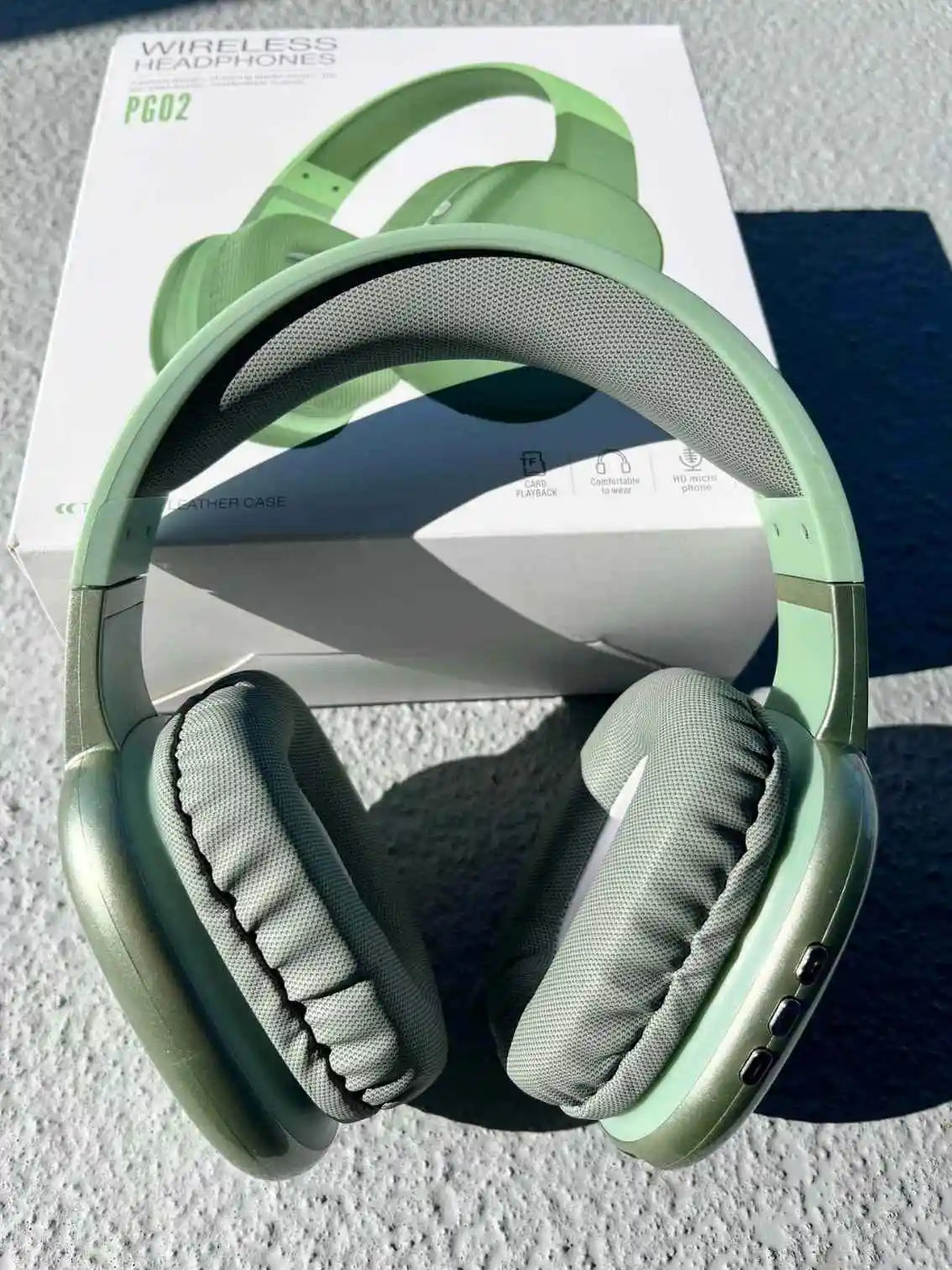 Green wireless PG02 Bluetooth headphones with microphone, displayed with product packaging in the background.