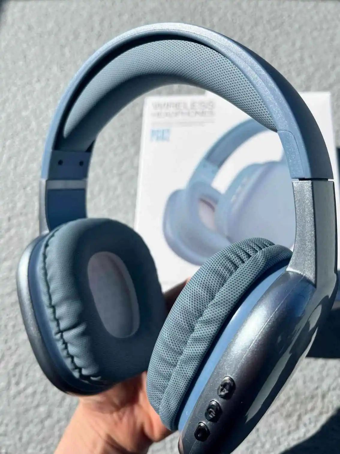 Close-up of blue wireless PG02 Bluetooth headphones in hand, with product packaging in the background.